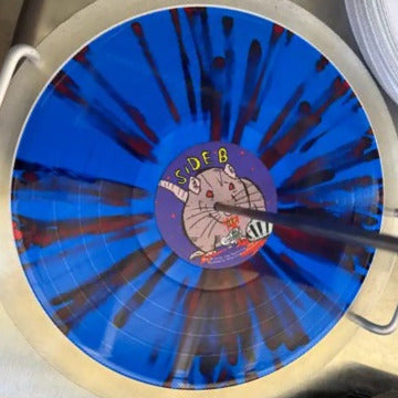 A close-up of a vinyl record with a blue and red splatter pattern, featuring a cartoon rat in the center and the text 'SIDE B'.